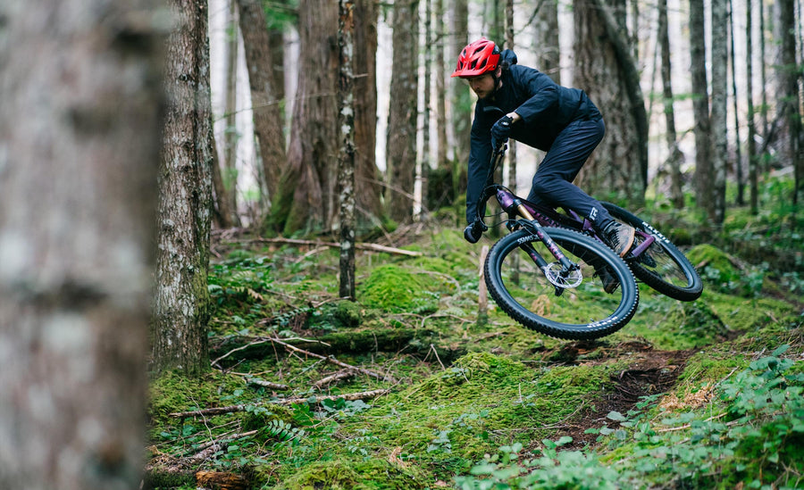 A man in a red helmet, jumping his Spur mountain bike down a forest track