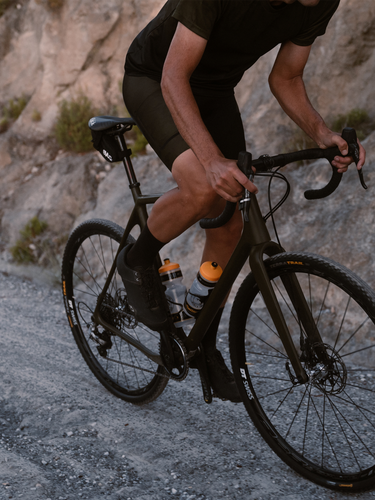 A man riding a black bike, showing close up of Continental brand tyres on a gravel road.